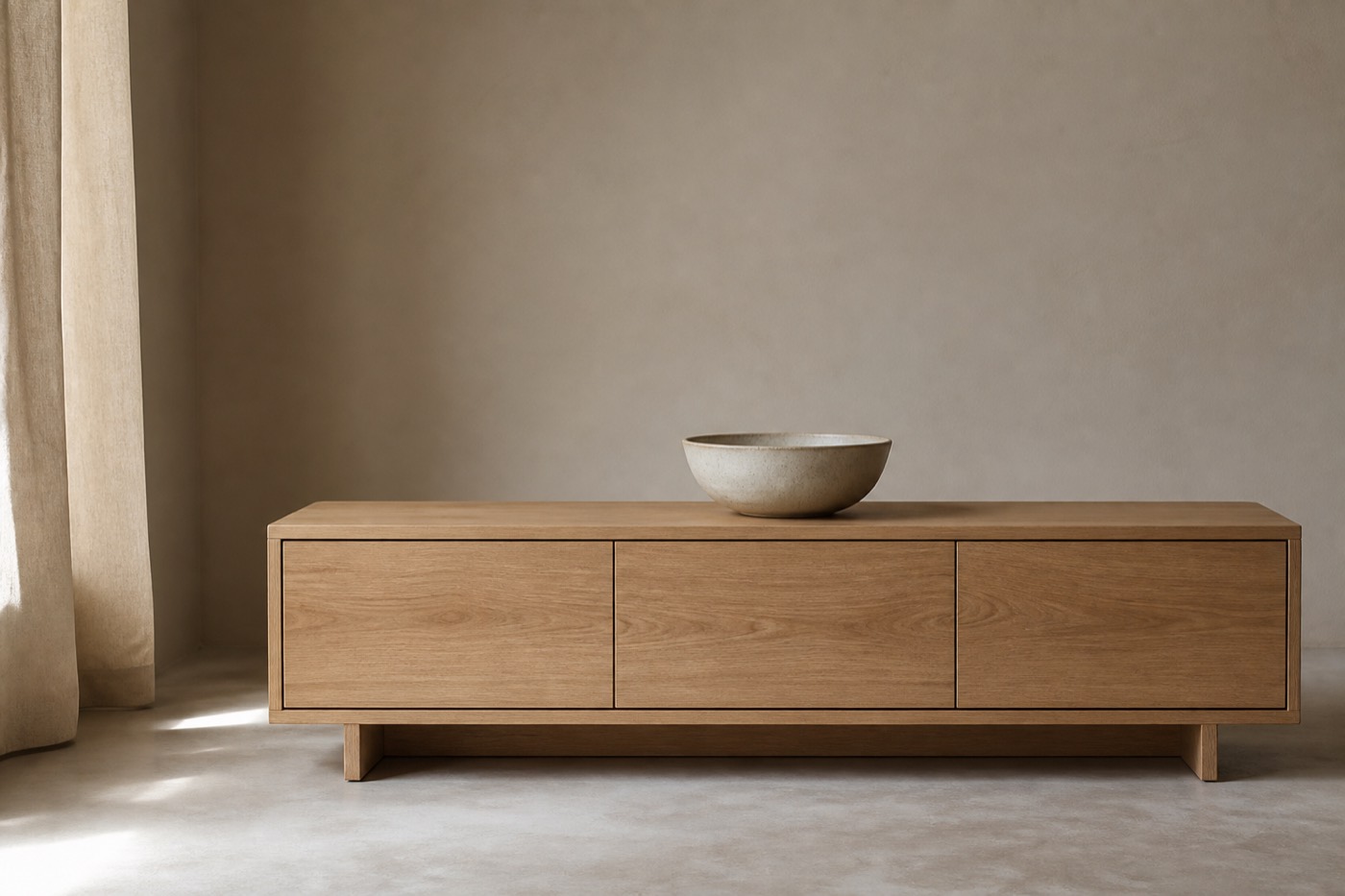 Låg sideboard i ljus ek med räta, handtagsfria luckor och en ensam keramikskål på toppen