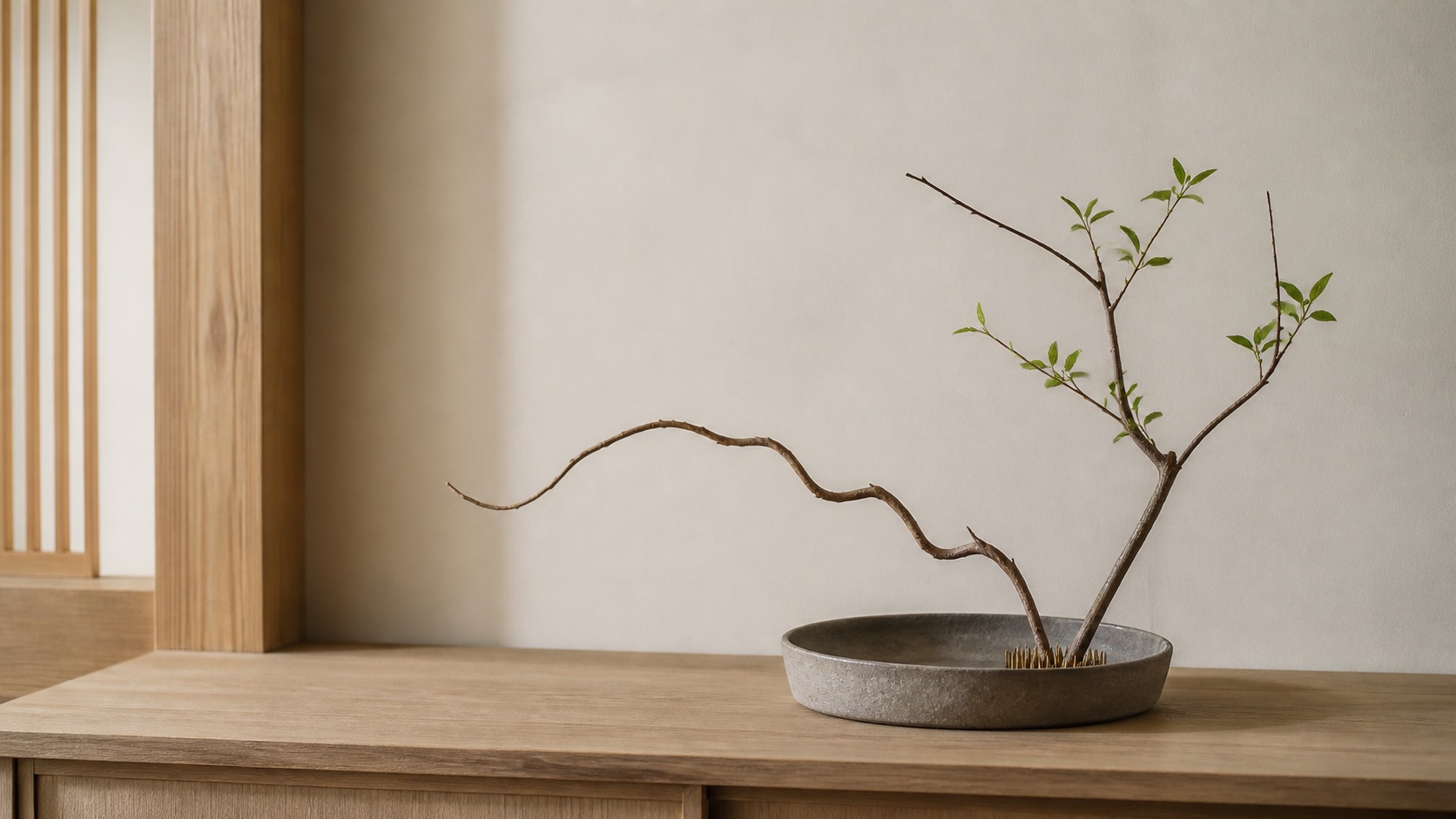 Ikebana: ett fåtal grenar i en låg keramikskål med kenzan, japandi-arrangemang med tomrum